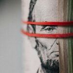 Close-up of rolled-up US currency secured with a red band, representing the financial impact of a writ of execution.