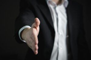 A lawyer extending his hand for a handshake after being hired, on a dark background.