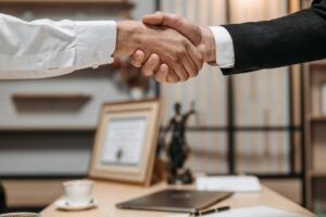 Two individuals shake hands over a desk in a law office, indicating agreement on working together for debt collection.