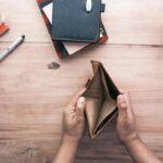 An overhead view of a man's hands resting on a wooden desk holding open an empty wallet, illustrating bankruptcy.