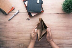 An overhead view of a man's hands resting on a wooden desk holding open an empty wallet, illustrating bankruptcy.