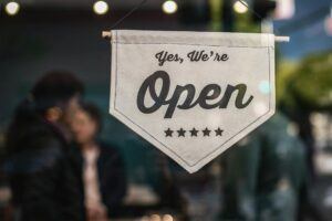 Sign reading 'Yes, We're Open' hanging in a small business window, representing business operations and challenges such as debt collection.