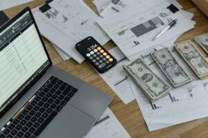 Workspace with a laptop, financial documents, a calculator on a smartphone, and stacks of cash, representing commercial debt recovery processes.