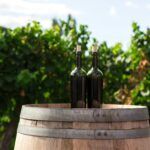 Two wine bottles on a wooden barrel in a vineyard setting, reflecting financial challenges and the role of debt collection in the wine industry.