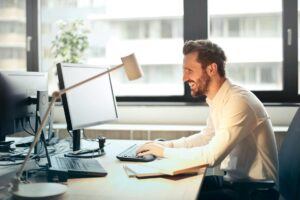 A business professional working at a desk, smiling, representing effective financial controls and collection strategies to safeguard staffing firms from accumulating bad debt.