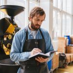 Franchise business owner reviewing notes in a warehouse setting with coffee roasting equipment