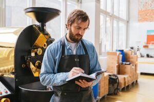 Franchise business owner reviewing notes in a warehouse setting with coffee roasting equipment