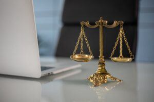 Brass balance scale placed beside a laptop on a glass desk, symbolizing justice, legal practice, and debt collection enforcement in a professional setting.