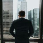 Man in a suit standing at a window overlooking a city skyline, symbolizing strategic decision-making and the weight of delayed judgment enforcement.
