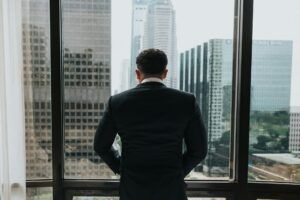 Man in a suit standing at a window overlooking a city skyline, symbolizing strategic decision-making and the weight of delayed judgment enforcement.