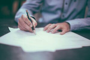 Close-up of a person in formal attire signing legal documents on a desk, representing the domestication and enforcement of sister-state judgments by legal counsel in California
